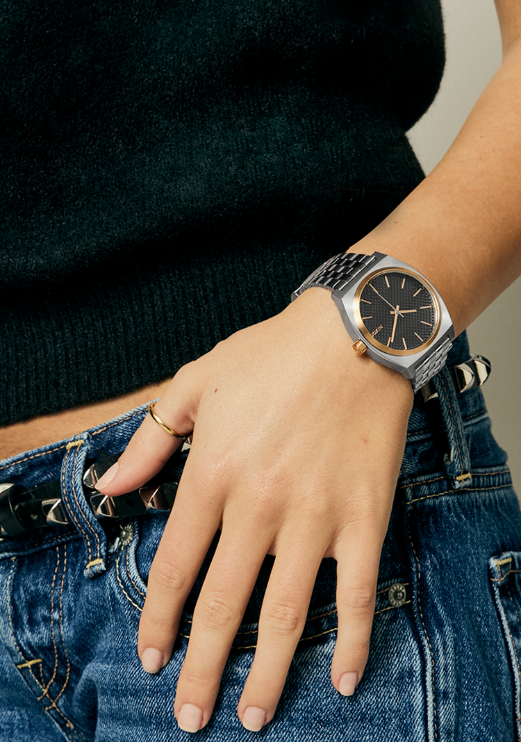 Woman wearing a Nixon Time Teller watch with her hand on her jeans